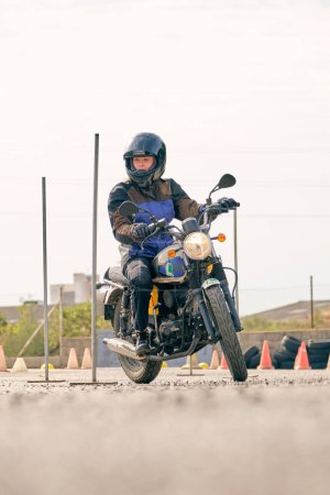 Foto de Nivel del suelo de la motociclista femenina montar en moto en el aeródromo de asfalto con obstáculos de metal y conos de naranjas - Imagen libre de derechos