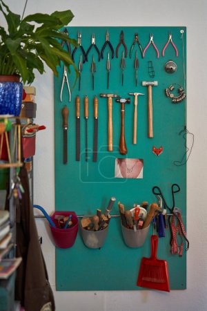 Téléchargez les photos : Ensemble de pinces coupeurs de fil limes et marteaux de banc suspendus en rangée sur le panneau vert sur le mur dans l'atelier d'orfèvrerie traditionnelle - en image libre de droit