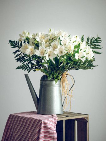 Photo for Bunch of fresh white Alstroemeria flowers placed in metallic watering can vase on table against gray background - Royalty Free Image