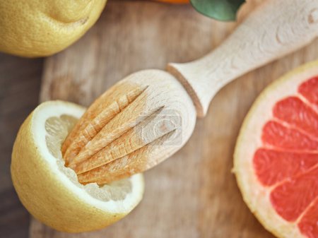 Foto de De arriba la mitad del limón con el exprimidor de madera manual a la tabla de cortar con el trozo del pomelo fresco en la cocina clara - Imagen libre de derechos