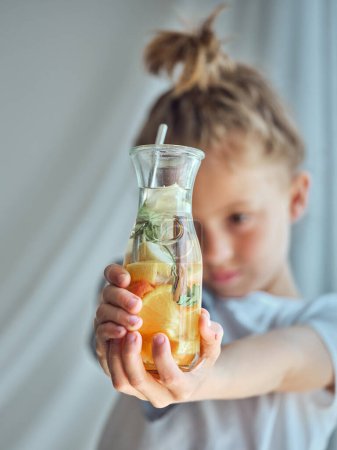 Téléchargez les photos : Concentration douce de l'enfant montrant un verre de limonade savoureuse faite de divers agrumes et épices - en image libre de droit