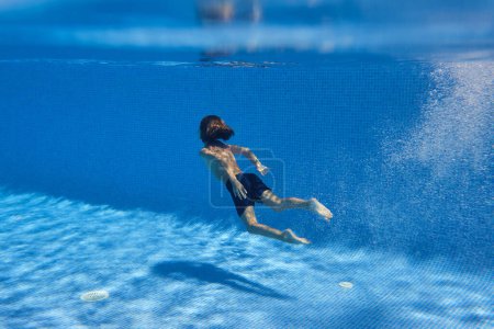 Foto de Por detrás de un niño anónimo rodeado de burbujas de aire que se sumergen en la piscina de azulejos en el complejo durante las vacaciones de verano - Imagen libre de derechos