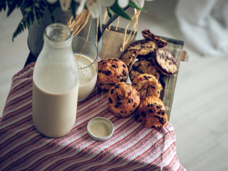 Foto de Composición de alto ángulo de deliciosa pastelería casera y botella de leche colocada cerca de jarrón con flores en caja de madera con tela - Imagen libre de derechos