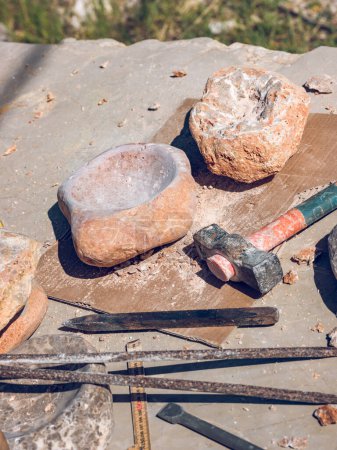Foto de Desde arriba de cuencos de piedra hechos de roca sólida colocados en el banco de trabajo cerca de martillo y cinceles en el taller al aire libre en el día soleado - Imagen libre de derechos
