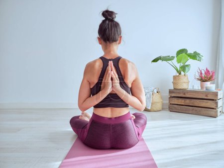 Photo for Back view of anonymous female in activewear sitting in Padmasana posture with prayer hands behind back during meditation on mat - Royalty Free Image
