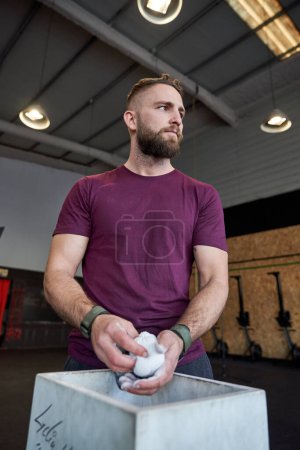 Photo for Low angle of serious bearded male in activewear using magnesia while preparing for workout and looking away - Royalty Free Image