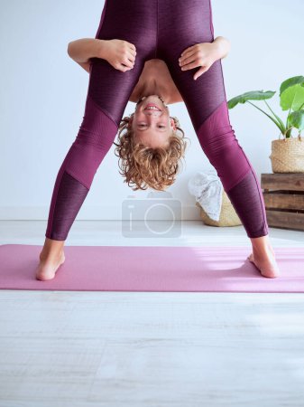Téléchargez les photos : Mère méconnaissable en vêtements de sport debout sur le tapis violet et soulevant fils joyeux tout en pratiquant le yoga ensemble à la maison - en image libre de droit