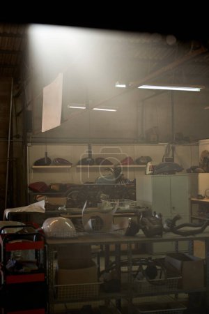 Foto de Interior del garaje oscuro con la luz que viene a través del techo que contiene varios suministros de reparación en los estantes y banco de trabajo de metal - Imagen libre de derechos