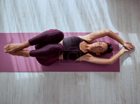 Téléchargez les photos : Vue du dessus corps entier de paisible pieds nus femme faisant Supine table asana sur tapis pendant la séance de yoga dans la salle de lumière - en image libre de droit