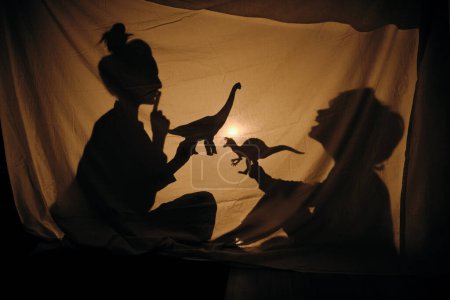 Foto de Vista lateral de mamá mostrando gesto shh mientras juega con su hijo con dinosaurios en el teatro de sombras - Imagen libre de derechos