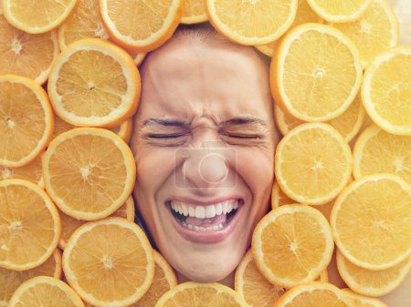 Photo for Overhead face of scared female frowning and shouting in large heap of fresh orange slices - Royalty Free Image