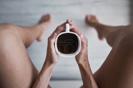 Photo for From above anonymous female holding black coffee cup in clasped hands while sitting and leaning on legs at home - Royalty Free Image