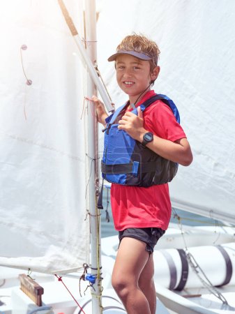 Photo for Positive male child in safety vest and cap smiling and looking at camera while standing on yacht during summer vacation - Royalty Free Image