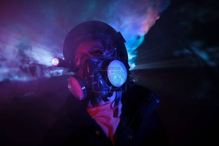Photo for Thug in protective respirator with exhaust filters and bright glowing flashlight standing in dark studio with fume during robbery - Royalty Free Image