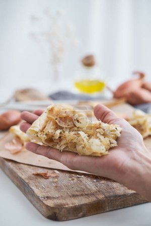Photo for Hand of crop unrecognizable person holding slice of baked tasty onion tart at table with cutting board in light kitchen - Royalty Free Image