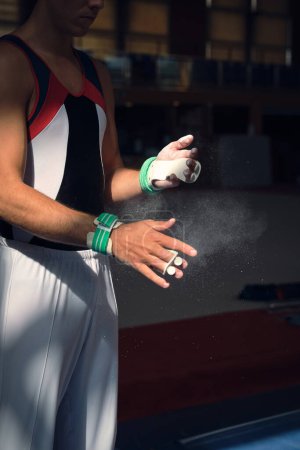 Foto de Deportista irreconocible preparándose poniendo magnesio en sus manos para hacer los ejercicios de gimnasia deportiva. - Imagen libre de derechos