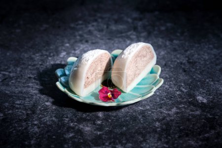 High angle of traditional Japanese mochi dessert with sweet jam sprinkled with sugar powder served on small plate placed on black marble table