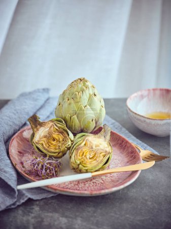 Foto de Sabroso brote de alcachofa verde saludable con hojas servidas en el plato con cubiertos en la mesa con toalla gris en la cocina ligera - Imagen libre de derechos