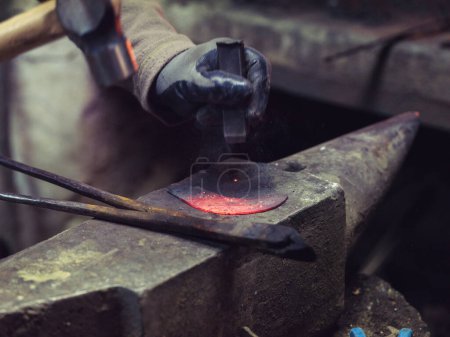 Photo for Unrecognizable male blacksmith forging piece of hot iron placed on anvil in forge workshop - Royalty Free Image