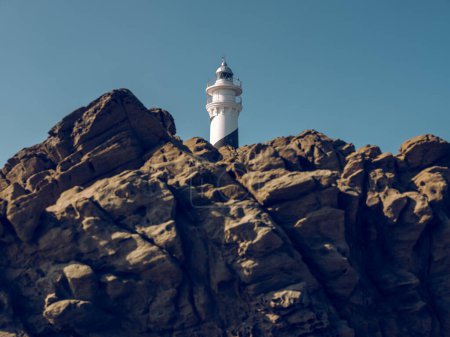 Photo for From below of picturesque landscape of white lighthouse located on top of rough rocky cliff in highland against cloudless blue sky - Royalty Free Image