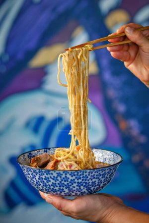 Foto de Cultivo irreconocible persona agarrando fideos con palillos mientras come tazón de deliciosa sopa de ramen en el restaurante asiático - Imagen libre de derechos