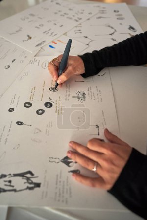 Foto de Alto ángulo de cultivo anónimo talentoso diseñador femenino dibujo boceto de diferentes accesorios en papel en taller de joyería - Imagen libre de derechos