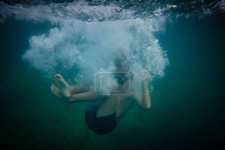 Foto de Vista lateral de cuerpo completo del niño en el mar con burbujas de aire y agua clara durante el viaje de verano en un resort tropical - Imagen libre de derechos