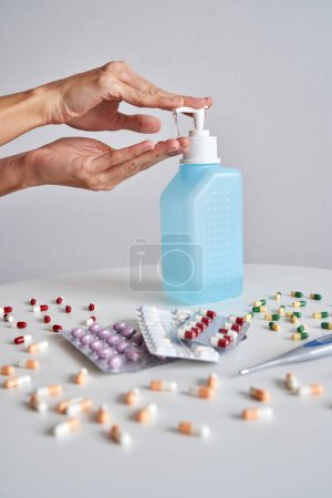 Photo for Hands of crop faceless person applying antibacterial gel on hand near abundance of pills during coronavirus pandemic on white background - Royalty Free Image