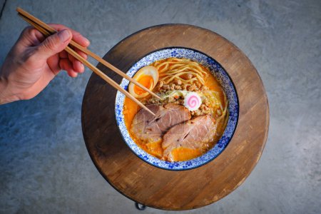 Photo for Top view of crop unrecognizable person holding chopsticks while eating delicious Japanese ramen soup with noodles and pork meat garnished with egg and narutomaki - Royalty Free Image