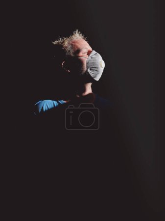 Foto de Vista lateral del molde macho rubio en máscara respiradora protectora y con ojos cerrados en oscuridad sobre fondo negro iluminado por la luz del sol - Imagen libre de derechos