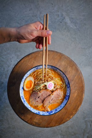 Téléchargez les photos : D'en haut de la culture personne sans visage manger traditionnelle asiatique soupe de nouilles avec de l'omble de porc siu et oeuf servi dans un bol sur une planche en bois - en image libre de droit