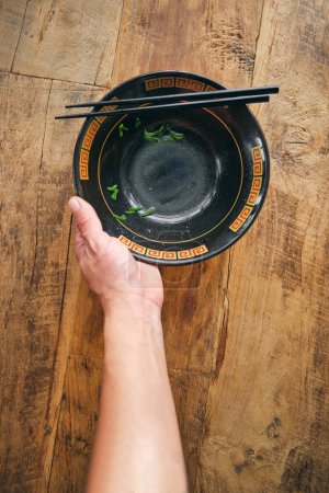 Photo for Overhead view of crop unrecognizable person with dirty bowl and food sticks on wooden table - Royalty Free Image