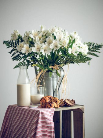 Téléchargez les photos : Composition de cupcakes et bouteille de lait placée près du bouquet de fleurs blanches sur boîte en bois avec chiffon sur fond blanc - en image libre de droit