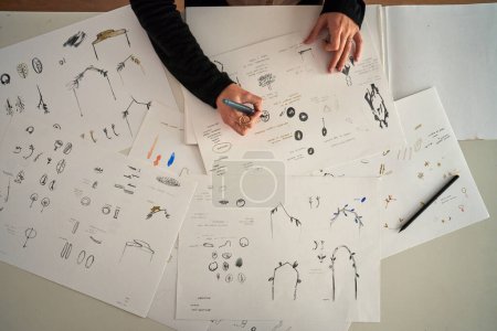 Téléchargez les photos : Vue du dessus de la récolte anonyme femme bijoutier dessin croquis d'accessoires créatifs sur papier en atelier d'artisanat - en image libre de droit