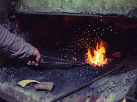Photo for Crop unrecognizable male blacksmith using tong while melting iron in furnace during forging process in traditional workshop - Royalty Free Image