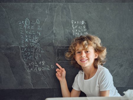 Téléchargez les photos : Enfant heureux regardant la caméra et pointant vers les équations mathématiques écrites sur un mur de pierre avec de la craie - en image libre de droit