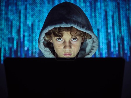 Seriöser Hacker mit Laptop blickt in Kamera auf verschwommenem Code-Hintergrund im dunklen Licht