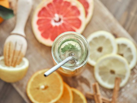 Photo for From above composition of bottle with zero waste straw filled with refreshing drink served with slices of various citruses and cinnamon sticks on wooden cutting board - Royalty Free Image