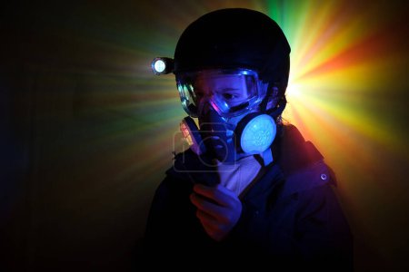 Photo for Robber in protective gas mask with walkie talkie in hand standing in mint with colorful neon illumination during illegal heist - Royalty Free Image