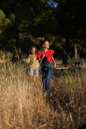 Photo for Happy preteen girl and boy in casual clothes walking on grassy field in countryside during weekend - Royalty Free Image