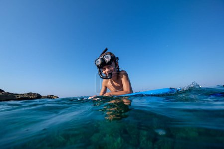 Téléchargez les photos : Joyeux garçon préadolescent en masque de plongée en apnée se préparant pour la plongée dans l'eau de mer bleue dans une journée ensoleillée sans nuages - en image libre de droit