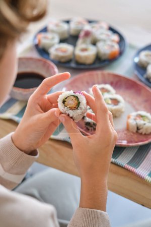 Photo for From above of crop anonymous preteen child sitting at table with delicious sushi rolls in kitchen at home - Royalty Free Image