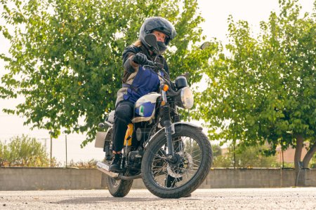 Foto de Nivel del suelo de la motociclista femenina en casco de protección a caballo motocicleta moderna en el motodromo en el día soleado - Imagen libre de derechos