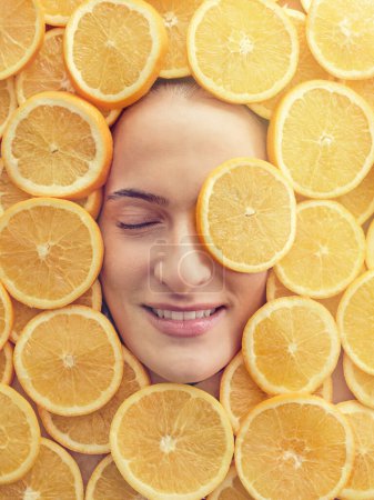 Foto de Vista superior de montón de rodajas de naranja fresca con la cara de la mujer en reposo en el centro - Imagen libre de derechos