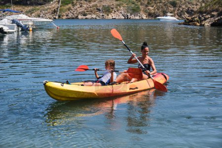 Foto de Madre con hijo remando colorido kayak con paletas en la superficie ondulante del agua durante el viaje en el soleado día de verano en España - Imagen libre de derechos