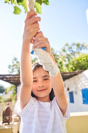 Photo for Portrait of adorable preteen kid in white clothes hanging on swing rope and looking at camera in sunny summer day - Royalty Free Image