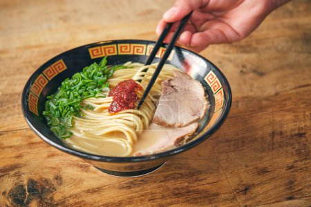 Téléchargez les photos : Personne sans visage avec des bâtonnets de nourriture et savoureuse soupe de nouilles japonaises avec salsa de tomate et tranches de porc dans le bouillon - en image libre de droit
