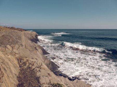 Téléchargez les photos : D'en haut de la mer bleue mousseuse lavant la côte rocheuse avec des falaises sous un ciel bleu sans nuages - en image libre de droit