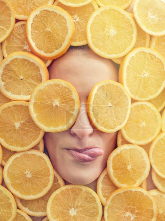 Foto de Vista superior de la cara femenina en trozos de naranjas frescas lamiendo labios con rebanadas en los ojos - Imagen libre de derechos