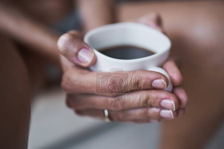 Foto de Cosecha irreconocible hembra sosteniendo taza de café caliente mientras está sentado en casa y las manos calientes durante el desayuno - Imagen libre de derechos
